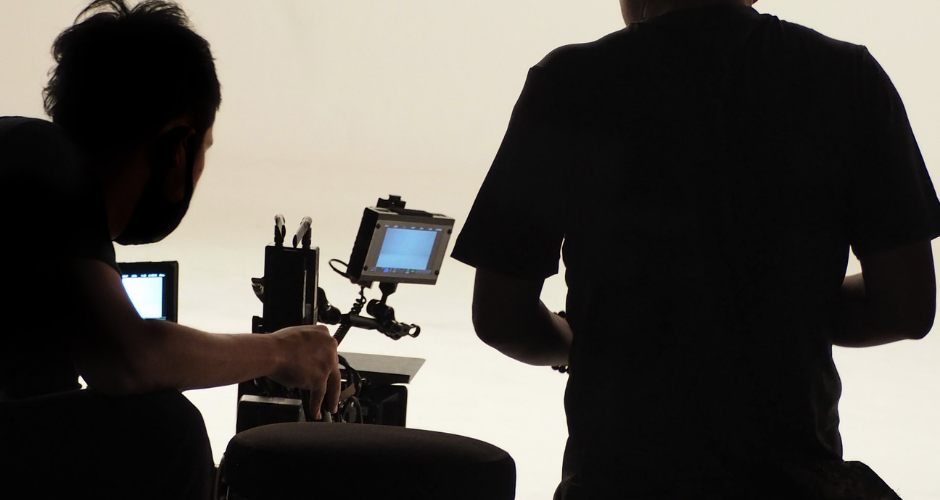 Two videographers adjusting professional camera equipment on a studio set with backlighting.