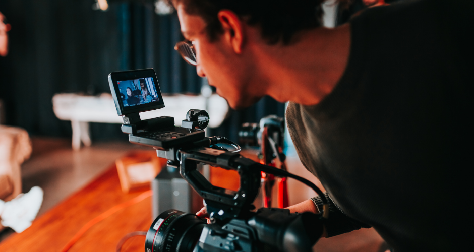 Videographer focusing a professional cinema camera on a subject during an indoor video shoot.
